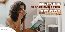 A woman sitting in her bed, reading a book and drinking tea
