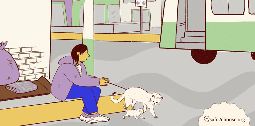 Una persona sentada en la acera con un gato y un gatito cerca, rodeada de bolsas y mantas. El entorno parece ser una zona urbana con edificios al fondo.
