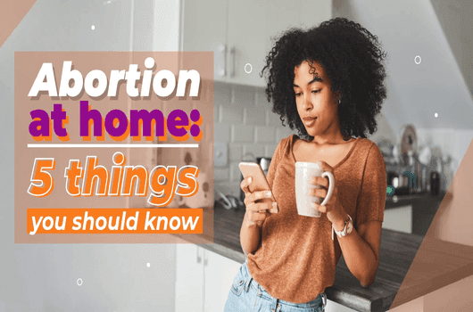 Woman in a kitchen holding a phone and mug, reading a screen. Text overlay: "Abortion at home: 5 things you should know." Relaxed atmosphere.